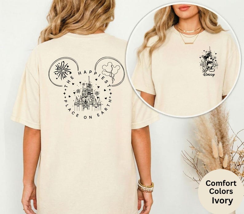 May include: Ivory-colored t-shirt featuring a black graphic of a castle, fireworks, and balloons in the shape of Mickey Mouse ears. The text "THE HAPPIEST PLACE ON EARTH" is printed around the castle. A smaller graphic of Mickey Mouse with the word "Daddy" is on the front.