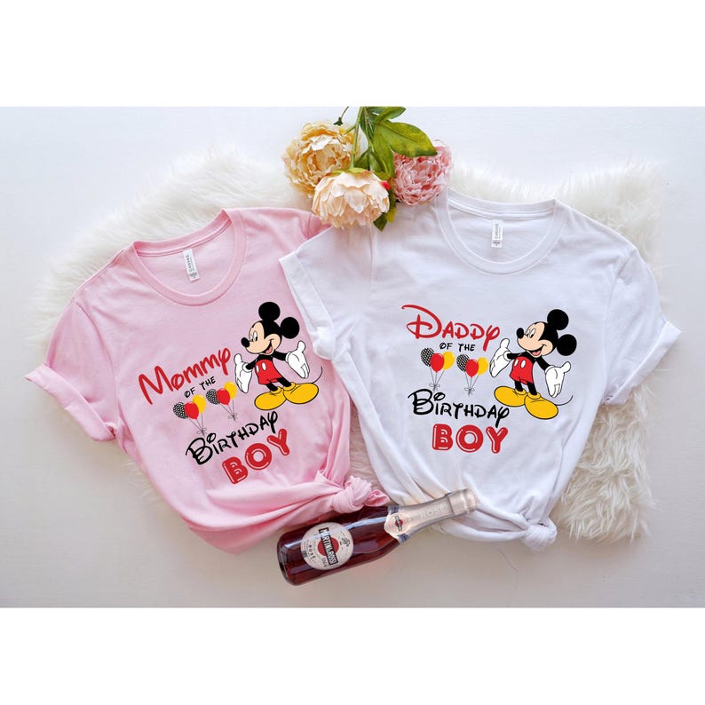 May include: Two t-shirts with a Mickey Mouse design. The pink shirt says "Mommy of the Birthday Boy" and the white shirt says "Daddy of the Birthday Boy".