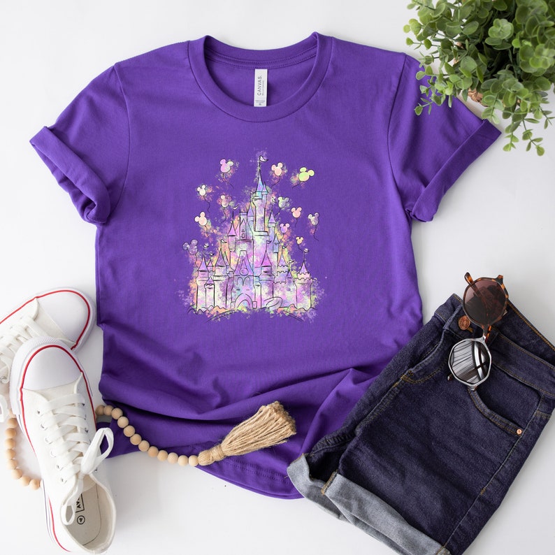 May include: Purple t-shirt featuring a watercolour illustration of Cinderella's castle with Mickey Mouse balloons.