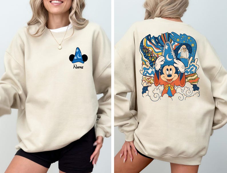 May include: A beige sweatshirt with a Mickey Mouse illustration wearing a sorcerer hat on the back. The front of the sweatshirt has a small Mickey Mouse ear and hat graphic with the word "Name" underneath.