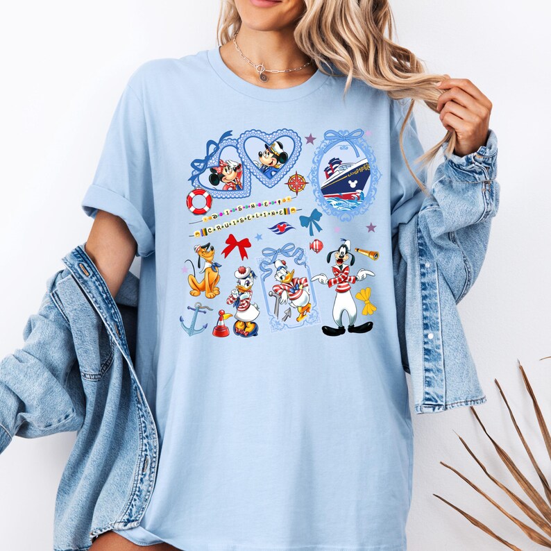 May include: Light blue t-shirt with a nautical theme featuring Mickey Mouse, Minnie Mouse, Donald Duck, Goofy, and Pluto. The shirt has a variety of nautical symbols, including anchors, stars, and a ship's wheel.