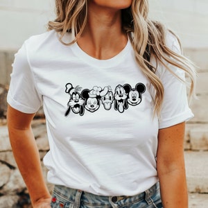 K&ouml;nnte beinhalten: Wei&szlig;es T-Shirt mit einem schwarz-wei&szlig;en Grafikdruck von Mickey Mouse, Minnie Mouse, Donald Duck, Goofy und Pluto. Die Figuren sind in einer Reihe angeordnet und l&auml;cheln.