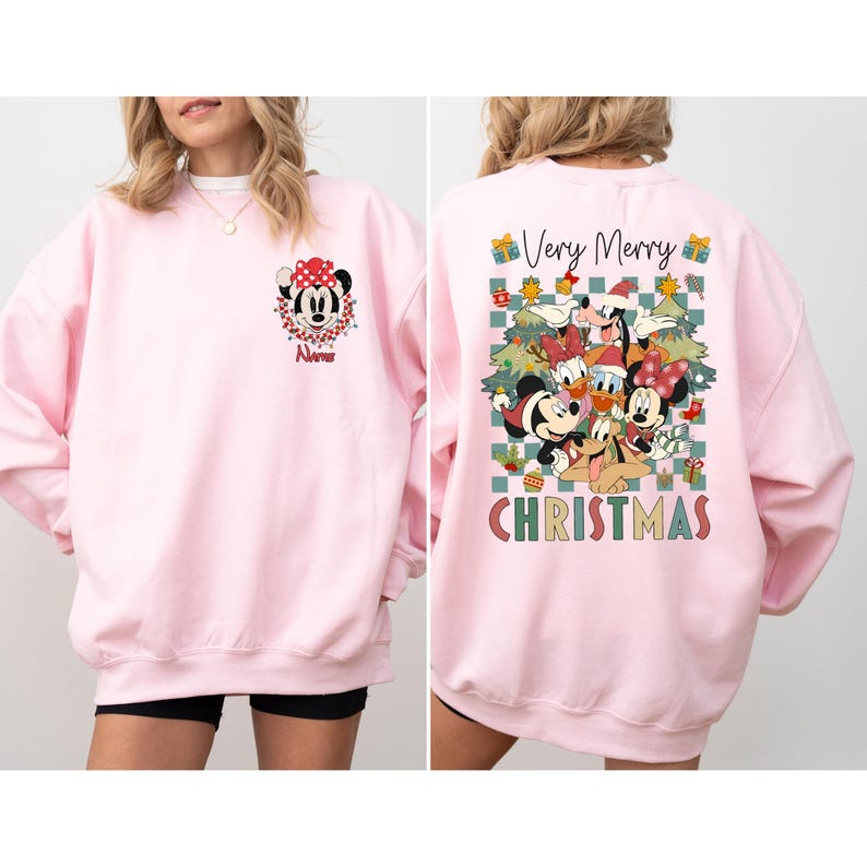 May include: A light pink sweatshirt featuring Minnie Mouse on the front with a red bow and the name "Name". The back of the sweatshirt has a graphic of Disney characters with the words "Very Merry CHRISTMAS".