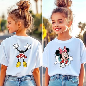 K&ouml;nnte beinhalten: Wei&szlig;es T-Shirt mit einem Minnie-Mouse-Motiv. Auf der Vorderseite ist Minnie Mouse, die aus einem Loch bricht, und auf der R&uuml;ckseite befindet sich eine Minnie-Mouse-Grafik. Das Design umfasst einen roten Polka-Dot-Rock und gelbe Schuhe.