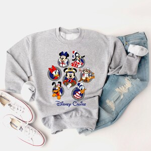 May include: A gray sweatshirt featuring Disney characters in sailor outfits. The design includes Mickey Mouse, Minnie Mouse, Donald Duck, Daisy Duck, Goofy, Pluto, and Chip and Dale. The words "Disney Cruise" are printed below the characters.