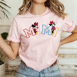May include: Pink t-shirt with a graphic of Mickey Mouse characters spelling out "MIMI" in colorful letters.
