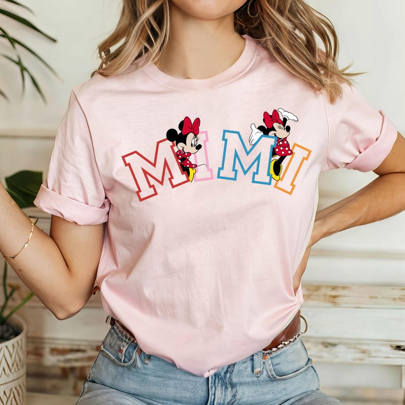 May include: Pink t-shirt with a graphic of Mickey Mouse characters spelling out "MIMI" in colorful letters.