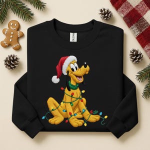 May include: Black sweatshirt with a cartoon Pluto design. The yellow dog is wearing a Santa hat and wrapped in Christmas lights. The design is festive and features a green collar. Christmas-themed clothing.