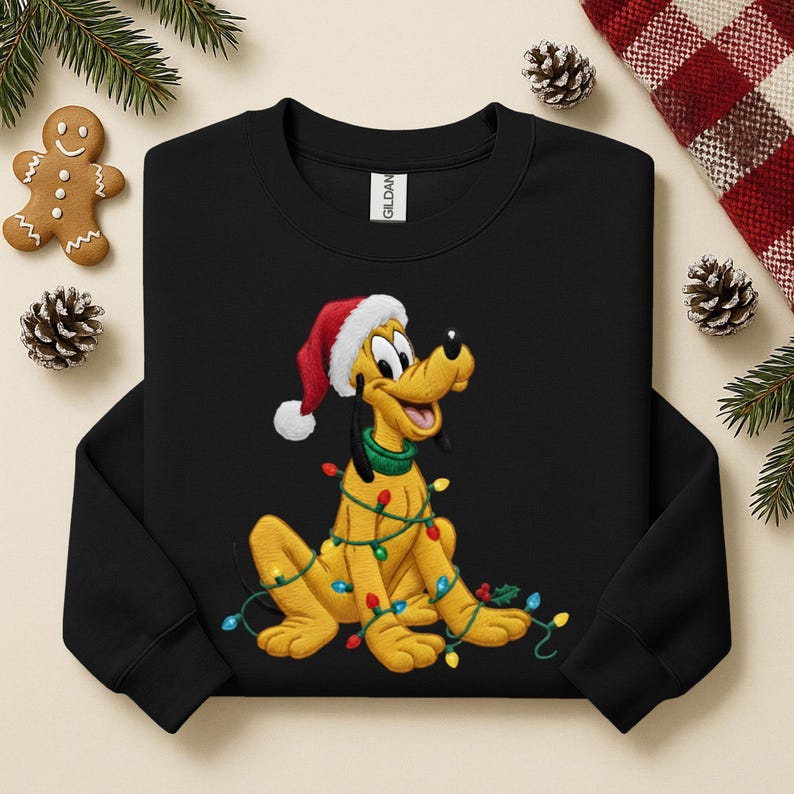 May include: Black sweatshirt with a cartoon Pluto design. The yellow dog is wearing a Santa hat and wrapped in Christmas lights. The design is festive and features a green collar. Christmas-themed clothing.