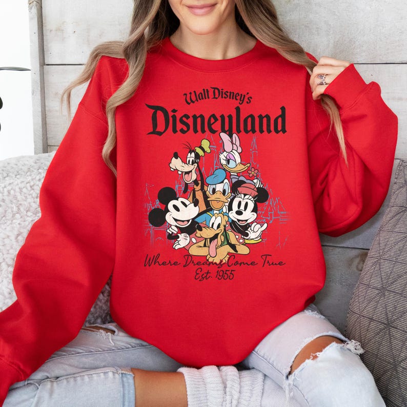 May include: A red sweatshirt featuring a graphic of Disney characters including Mickey Mouse, Minnie Mouse, Donald Duck, Goofy, and Daisy Duck. The text "Walt Disney's Disneyland" and "Where Dreams Come True Est. 1955" are printed on the front.
