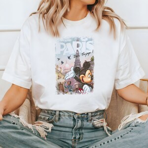 May include: White t-shirt with a vintage-style graphic of Mickey Mouse in front of the Eiffel Tower in Paris. The graphic includes the text "Disneyland Paris" and "Bon Voyage!"