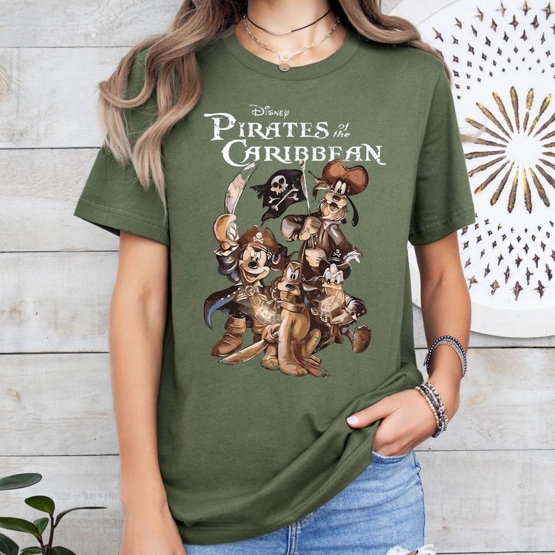 Pode incluir: Camiseta verde com uma estampa gr&aacute;fica de Mickey Mouse, Pateta e Donald Duck vestidos de piratas. O texto "Disney Pirates of the Caribbean" est&aacute; impresso acima dos personagens.