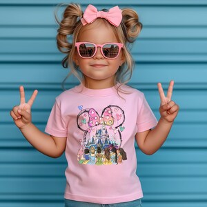 May include: A pink t-shirt with a graphic of Cinderella, Snow White, Ariel, Belle, and Rapunzel standing in front of Cinderella's castle. The graphic is surrounded by a Mickey Mouse head with a pink bow and balloons.