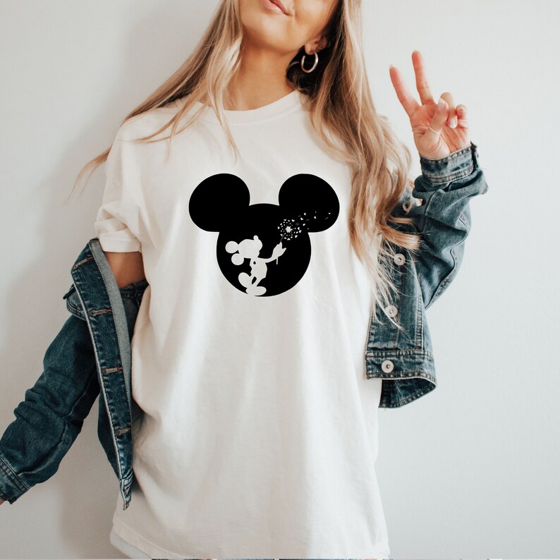 May include: White t-shirt with a black silhouette of Mickey Mouse blowing a dandelion. The silhouette is inside a black outline of Mickey Mouse's head.