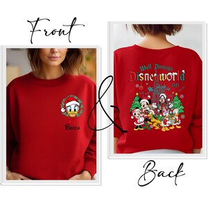 Op de afbeelding: Rode sweatshirt met Donald Duck in een kerstmuts en krans op de voorkant, met de naam "Becca" eronder. De achterkant toont een Disney World-afbeelding met Mickey Mouse en andere personages, samen met de tekst "Walt Disney's Disneyworld 1971."