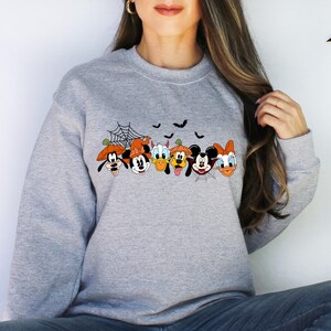 May include: A gray sweatshirt with a print of Mickey Mouse, Minnie Mouse, Donald Duck, Goofy, and Pluto dressed in Halloween costumes. The characters are lined up in a row with a spiderweb and bats above them.
