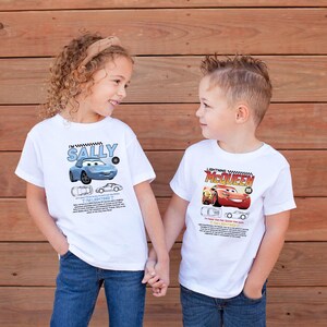 May include: Two children wearing white t-shirts with cartoon car graphics. One shirt features a blue car with the name "SALLY" and the text "I'M LIGHTNING". The other shirt displays "LIGHTNING McQUEEN" and a red car.