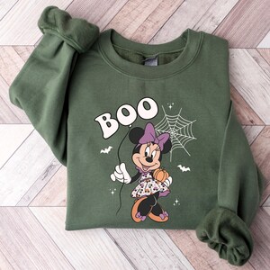May include: Green sweatshirt with a cartoon image of Minnie Mouse dressed in a purple and black dress holding a pumpkin. The text "BOO" is above her in a white balloon.