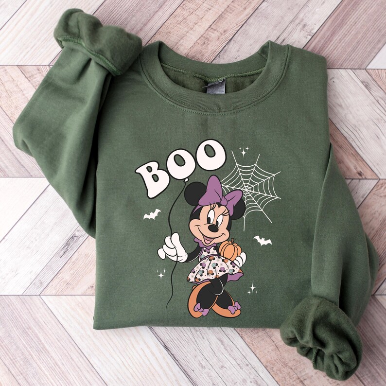 May include: Green sweatshirt with a cartoon image of Minnie Mouse dressed in a purple and black dress holding a pumpkin. The text "BOO" is above her in a white balloon.