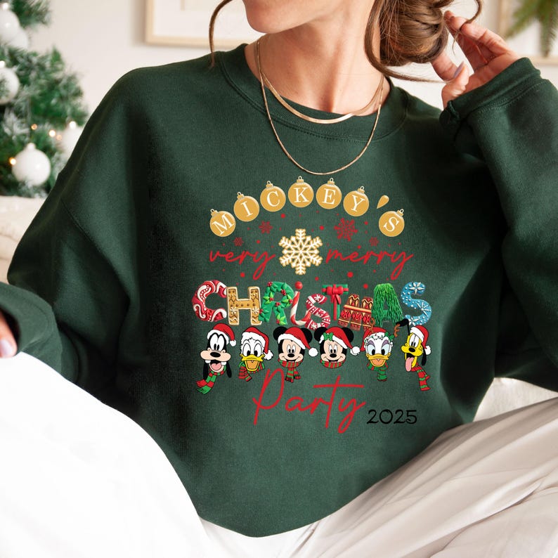 K&ouml;nnte beinhalten: Gr&uuml;ner Weihnachtspullover mit Mickey Mouse und seinen Freunden. Der Text lautet "Mickey's Very Merry Christmas Party 2025".