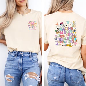 May include: Cream-colored t-shirt with a colorful graphic on the front and back. The front features a Minnie Mouse design with the text "Mrs. White." The back displays the phrase "Making Magic for Tiny Humans Every Day" with cartoon characters.