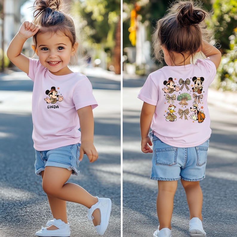 May include: A pink t-shirt with a cartoon image of Mickey Mouse wearing a safari hat and the word "Linda" printed on the front. The back of the shirt features a design with Mickey Mouse and other Disney characters in safari outfits.