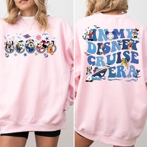 May include: Pink sweatshirt with a graphic of Mickey Mouse and friends on a cruise ship on the front and the text "In My Disney Cruise Era" on the back.