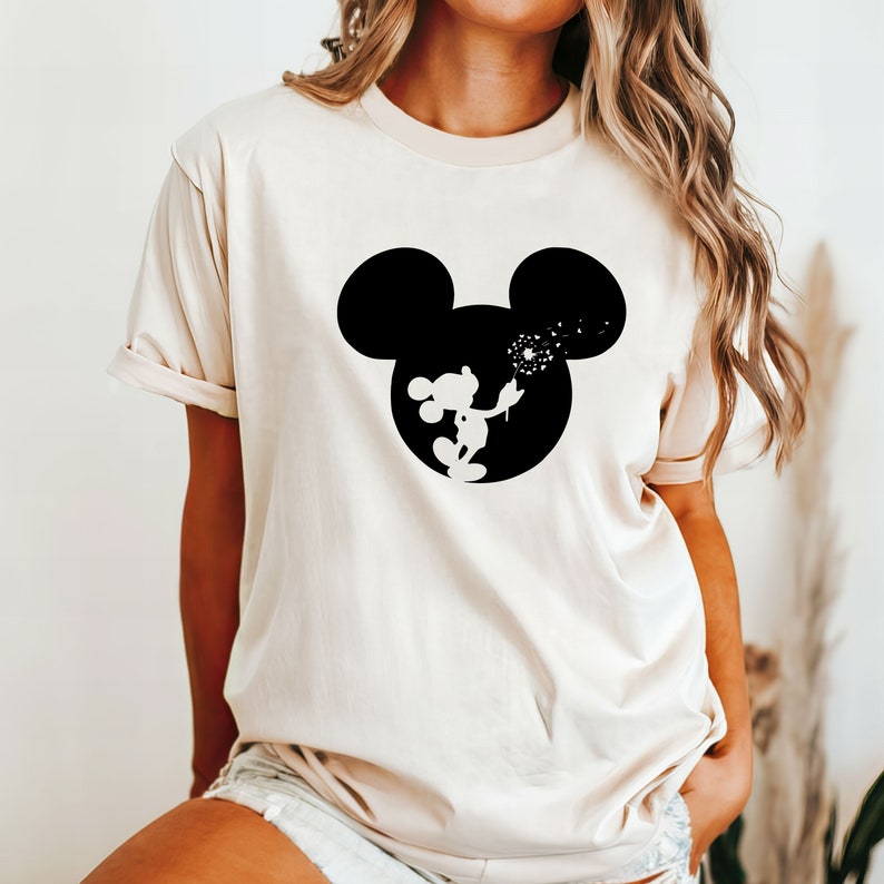 May include: A white t-shirt with a black silhouette of Mickey Mouse blowing on a dandelion. The silhouette is in a circle shape.