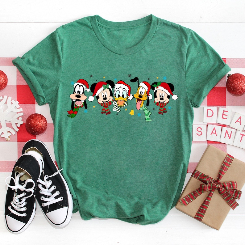 May include: Green t-shirt with a Christmas-themed design featuring Mickey Mouse, Donald Duck, Goofy, Pluto, and a character wearing a Santa hat.
