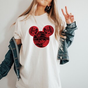 May include: White t-shirt with a red Mickey Mouse head design. The head is filled in with a black and white image of the Death Star from Star Wars.