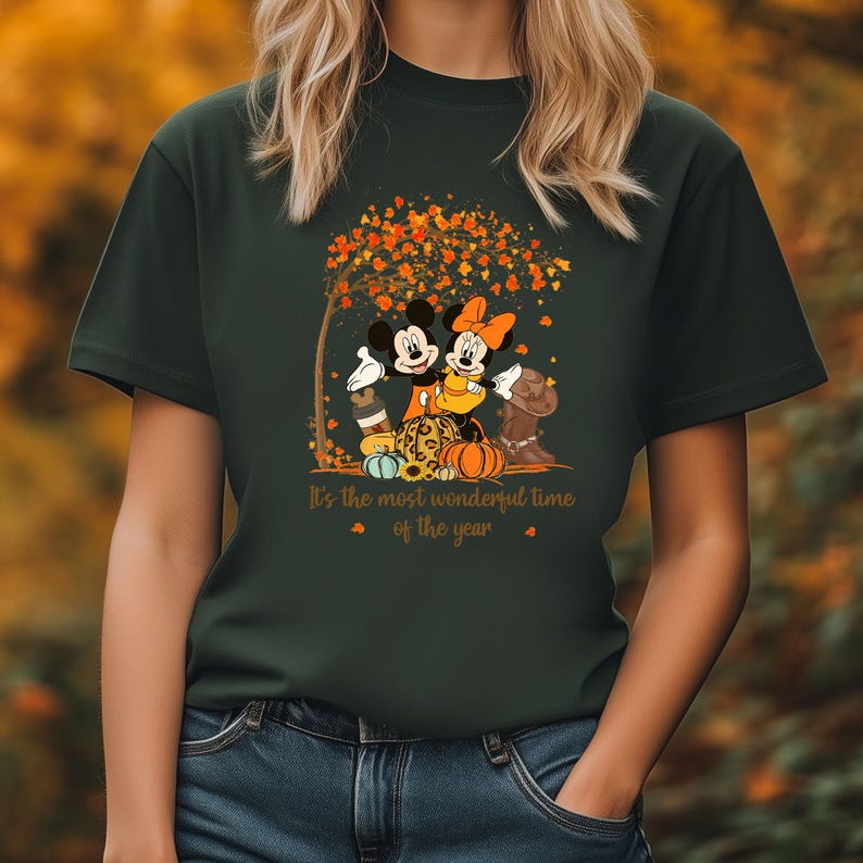 May include: Dark green t-shirt with a graphic of Mickey and Minnie Mouse beneath a tree with autumn leaves. The design includes pumpkins and the text "It's the most wonderful time of the year."