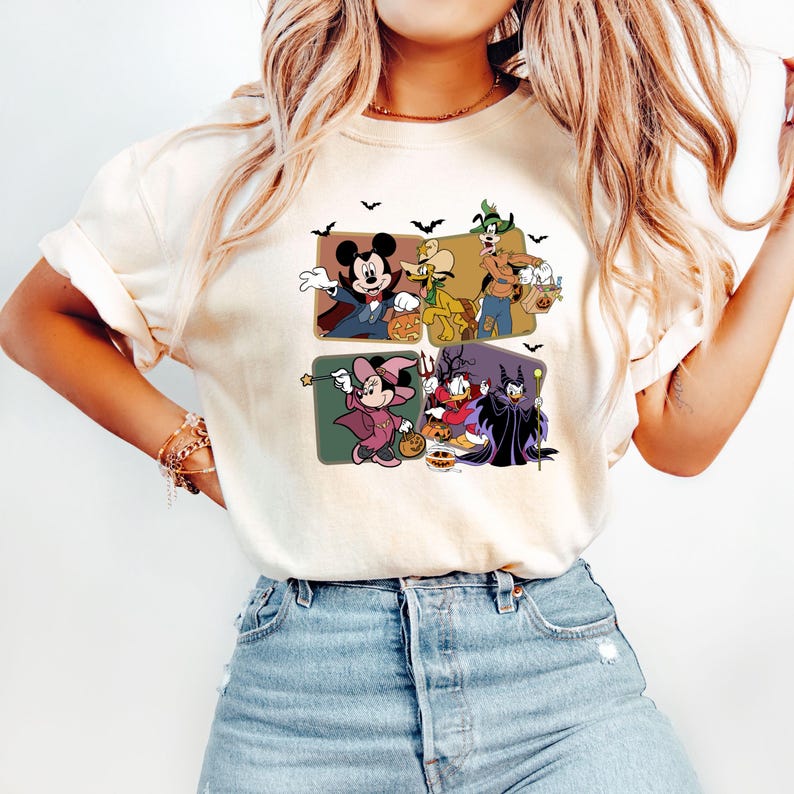 Puede incluir: Camiseta color crema con un dise&ntilde;o tem&aacute;tico de Halloween con Mickey Mouse, Minnie Mouse, el Pato Donald y otros personajes de Disney disfrazados. El dise&ntilde;o incluye murci&eacute;lagos y calabazas, perfecto para la temporada de sustos.