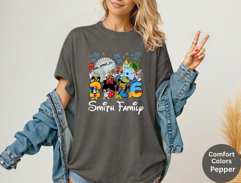 May include: Dark gray t-shirt featuring a colorful graphic with the numbers "2026" and Disney characters. The text "Smith Family" is below the graphic. The shirt has a crew neck and short sleeves.