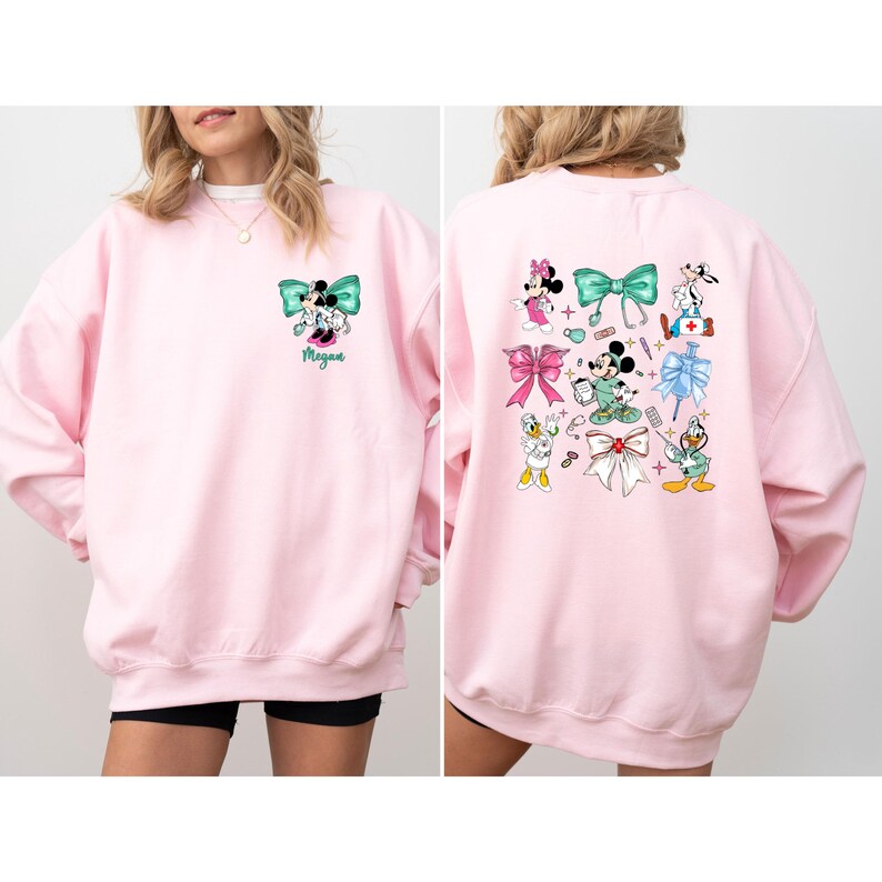 May include: A light pink sweatshirt featuring a Minnie Mouse and Mickey Mouse design with a teal bow. The back of the sweatshirt has multiple Disney character designs. The name "Megan" is printed below the front design.