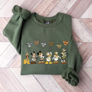 Pode incluir: Uma camisa de frio verde com uma estampa de personagens da Disney segurando bal&otilde;es com estampa de animais. Os personagens incluem Mickey Mouse, Donald Duck, Pateta e Pluto.
