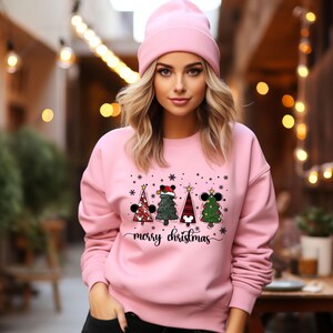 May include: Pink sweatshirt with a Christmas tree design featuring Mickey Mouse ears. The trees are decorated with ornaments and lights. The text "merry christmas" is printed below the trees.