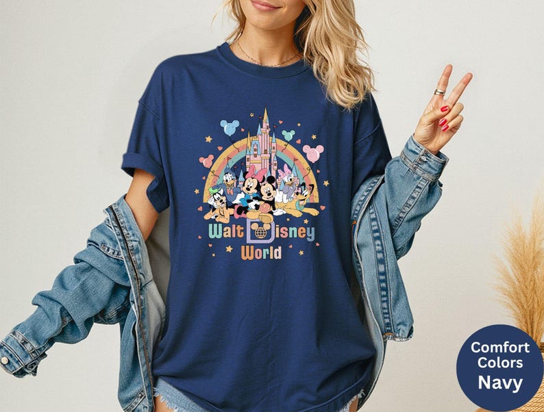 Puede incluir: Camiseta azul marino con un gr&aacute;fico colorido de personajes de Disney, un arco&iacute;ris y un castillo. El texto "Walt Disney World" se muestra debajo de los personajes. La camiseta tiene mangas cortas y cuello redondo.
