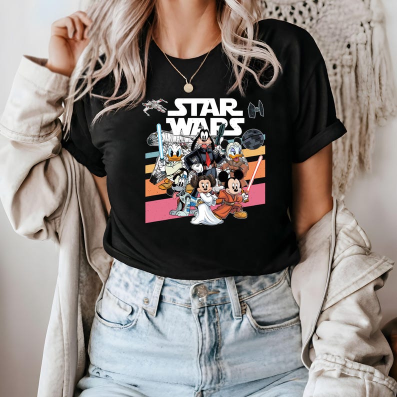K&ouml;nnte beinhalten: Schwarzes T-Shirt mit einer Grafik, die Disney-Figuren in Star Wars-Kleidung zeigt. Das Design umfasst Micky Maus, Minnie Maus, Donald Duck und Goofy, mit dem Star Wars-Logo.
