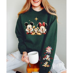 May include: Dark green sweatshirt featuring Mickey Mouse, Minnie Mouse, and Pluto in festive holiday attire. The sleeve displays additional Disney characters in Santa hats. A star graphic is above the characters.