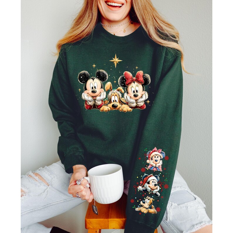 May include: Dark green sweatshirt featuring Mickey Mouse, Minnie Mouse, and Pluto in festive holiday attire. The sleeve displays additional Disney characters in Santa hats. A star graphic is above the characters.