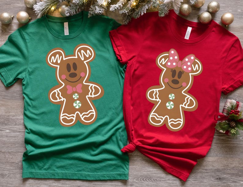May include: Two green and red t-shirts featuring a gingerbread Mickey Mouse and Minnie Mouse design. The Mickey Mouse shirt is green and the Minnie Mouse shirt is red.