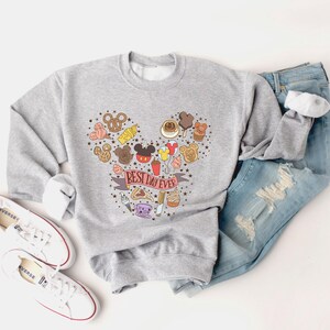 May include: A gray sweatshirt with a Mickey Mouse head design made up of various Disney-themed food and icons. The text "Best Day Ever" is written on a red ribbon.