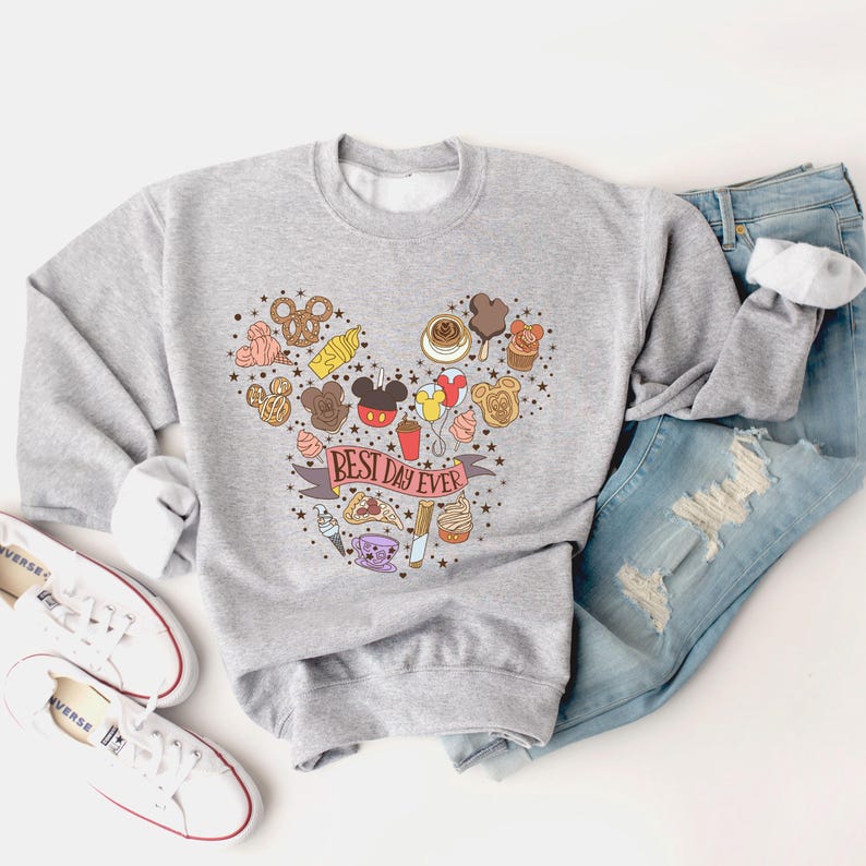 May include: A gray sweatshirt with a Mickey Mouse head design made up of various Disney-themed food and icons. The text "Best Day Ever" is written on a red ribbon.