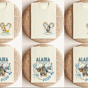 May include: Cream-colored t-shirts with Disney character graphics. One design features Mickey Mouse with "DAD 2023" in a Mickey Mouse ear frame. Another design says "ALASKA Disney Wonder 2025" with Mickey, Donald, and Goofy.