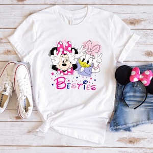 May include: White t-shirt with a graphic of Minnie Mouse and Daisy Duck with the word "Bestiies" in pink and blue letters.