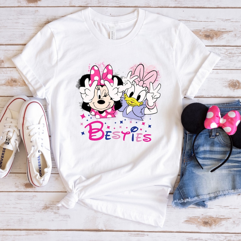 May include: White t-shirt with a graphic of Minnie Mouse and Daisy Duck with the word "Bestiies" in pink and blue letters.
