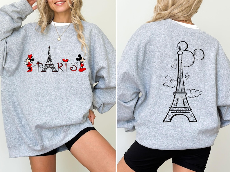 K&ouml;nnte beinhalten: Ein graues Sweatshirt mit einem Design mit dem Eiffelturm und dem Wort "Paris". Die Vorderseite des Sweatshirts zeigt Minnie- und Mickey Mouse-Figuren. Die R&uuml;ckseite des Sweatshirts hat eine schwarze Umrisszeichnung des Eiffelturms.