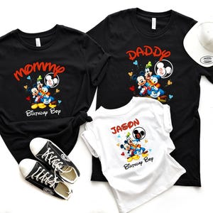 May include: Black t-shirts with Mickey Mouse, Donald Duck, and Goofy graphics. One shirt says "Mommy Birthday Boy", another says "Daddy & Two", and the third says "Jason Birthday Boy". A white baseball cap and black sneakers are also in the image.