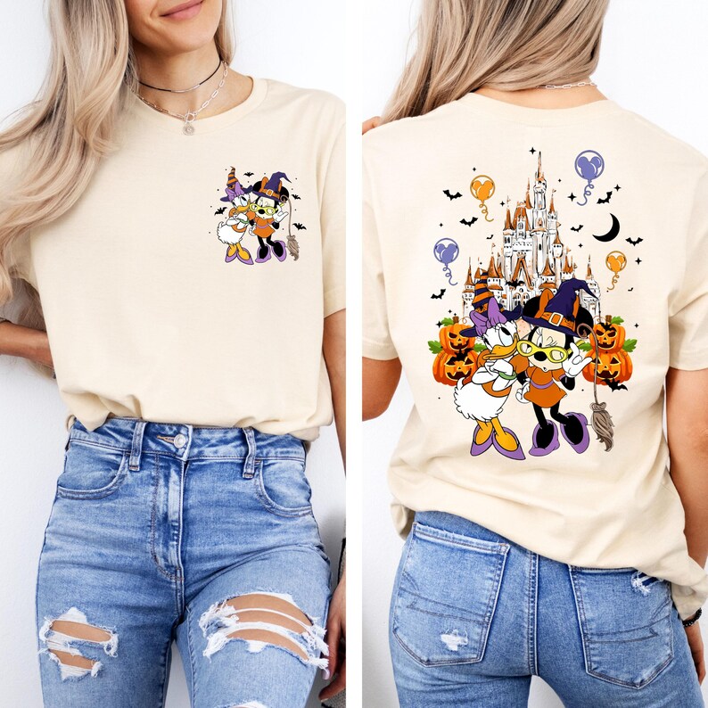 May include: Beige t-shirt featuring a Halloween-themed graphic of Mickey and Daisy Duck in witch costumes. The front has a small image, while the back showcases a larger design with a castle, pumpkins, and bats.