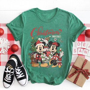 Op de afbeelding: Groen T-shirt met een kerstthema met Mickey en Minnie Mouse voor een rode auto. De tekst op het shirt luidt "Christmas on Main Street".